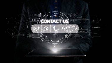 Profesyonel bir işadamı, elinde parlak bir tabletle karanlık bir ortamda modern iletişim yöntemlerini ve müşteri desteğini sembolize ederek ekranla temas kurar. Dörtgen