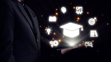 Profesyonel bir birey karanlık bir ortamda duruyor, parlak eğitim sembolleriyle bir tablet sergiliyor, bilginin ve sürekli öğrenmenin önemini vurguluyor. Dörtgen