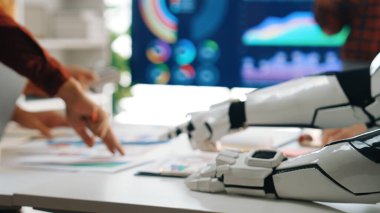 Modern ofis ortamında veri analizi ve strateji planlaması konusunda insanlarla işbirliği yapan bir robot kolunun yer aldığı fütüristik bir iş görüşmesi sahnesi. Noogenesis