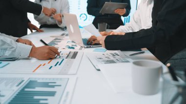 Strateji geliştirme üzerine odaklanan bir iş toplantısında, çeşitli profesyonellerden oluşan bir grup, bir dizüstü bilgisayardaki çizelge ve verileri analiz ederek çağdaş bir ofis ortamında işbirliği yapıyor. SACTR