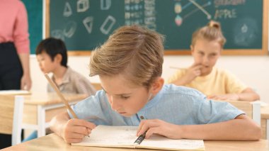 Çekici beyaz çocuk okulda matematik okurken kameraya bakıyor. Çeşitli şirin öğrenciler test yaparken öğretmen Asyalı çocuklara soru sorup tahtaya kağıt doğrultuyor. Pedagoji.