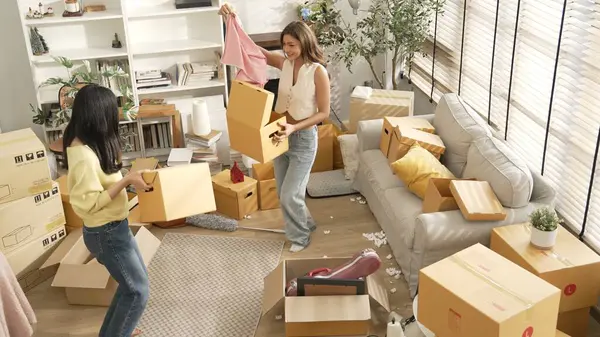 Taşınırken karton kutu taşırken birlikte dans eden mutlu çiftin üst görüntüsü. Çekici oda arkadaşı arkadaşına gösterirken kutudan bez toplarken müziğe yönelmiş. Yeniden yerleştirme. Myrmidon.