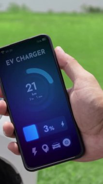 Akıllı telefon ekran akü durumu arayüzünü elinde tutan iş adamı akıllı EV mobil uygulama ile EV otomobili elektrik şarj istasyonundan doğal göl arka planı ile elektrik. İnceleyin.