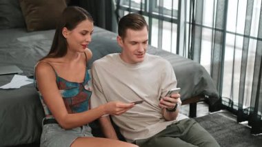 Genç çift, kredi kartıyla ödemek için internet üzerinden ödeme uygulaması ve dijital cüzdan kullanarak yatak odasında oturuyor. Mobil internet üzerinden alışveriş ve modern alımlar. Düzenle