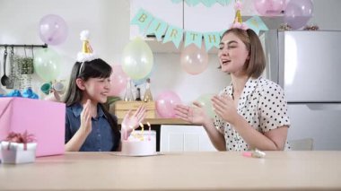 Çocuk ve beyaz anne birlikte doğum günü şarkısı söyleyip mumu üflüyorlar. Asyalı kız ve beyaz anne doğum gününü renkli balon ve hediyelerle süslenmiş yemek salonunda kutluyor. Pedagoji.