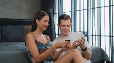 Genç çift, kredi kartıyla ödemek için internet üzerinden ödeme uygulaması ve dijital cüzdan kullanarak yatak odasında oturuyor. Mobil internet üzerinden alışveriş ve modern alımlar. Düzenle