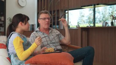 Grandfather and granddaughter eat french fries watch interesting entertainment on TV. Senior use technology communicate with young generation cross generation gap strengthen family bond. Divergence.