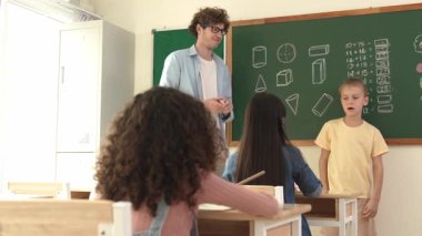 Profesyonel öğretmen konuşuyor ve sınıfta Asyalı çocuğa fikrini açıklıyor. Sınıfın önünde karatahta matematik dersiyle dikilmiş beyaz öğrenci dinleme eğitmeni. Pedagoji.