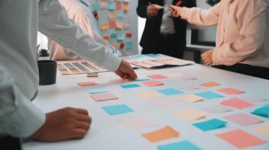 Dinamik bir ekip, masa üzerindeki renkli yapışkan notlarla çevrili modern bir ofiste beyin fırtınası ve planlama sürecini gösteren bir işbirliği içinde. SACTR