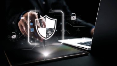 Bir iş adamı, çağdaş bir ofis ortamında modern teknoloji ve veri korumasını gösteren bir siber güvenlik kalkanını görselleştirmek için bir tabletle etkileşime girer. Dörtgen