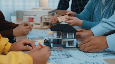 Çeşitli mimari ekipler, modern bir çalışma masasındaki planların ve planlama malzemelerinin yanında bir evin detaylı ölçekli modelini inceleyerek yaratıcı bir oturuma girişiyor. SACTR