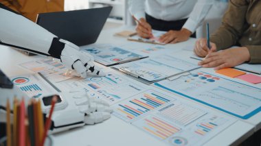 Veri analizi yapan bir insan ve robotu gösteren yaratıcı bir işbirliği sahnesi, canlı bir ofis ortamında teknoloji ve insan öngörüsü arasındaki sinerjiyi vurguluyor. Noogenesis