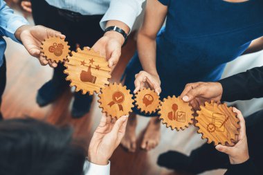 Bir grup profesyonel, iş ortamında işbirliği ve ortak hedefleri vurgulayarak strateji, büyüme ve takım çalışmasını temsil eden çeşitli sembollere sahip ahşap viteslere sahip. Dostluk