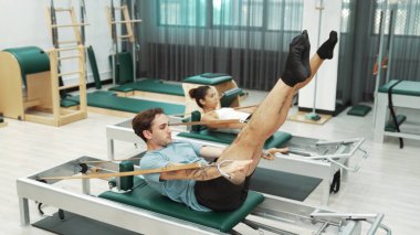 Bir grup müşteri, yenilikçi bir makinede bacak yükseltme işlemi yapıyor. Pilates partneri reformcu pozu veriyor ve egzersiz sırasında dengeyi geliştirmek ve koordinasyonu arttırmak için kayış takıyor. Alışkanlık.