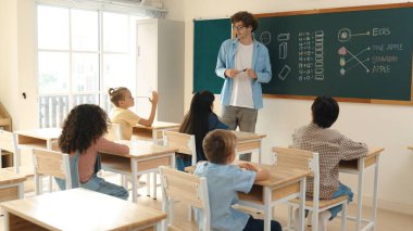 Çeşitli ilkokul öğrencileri öğretmenleri çocuğa bakarken sınıfta yürüyorlar. Profesyonel eğitmen tahtaya çıkıp öğretmenlik yapmaya hazırlanırken sevimli çocuklar sınıfa katılıyor. Pedagoji.