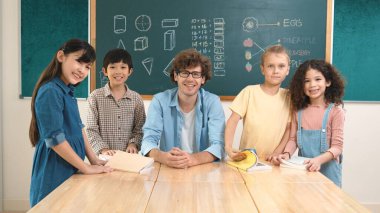 Profesyonel Kafkas öğretmeni ve çeşitli öğrenciler kameraya bakarken mutlu okul çocuğu gülümsüyor. Sınıfın önünde dururken gülümseyen bir grup çok kültürlü çocuk. Eğitim. Pedagoji.