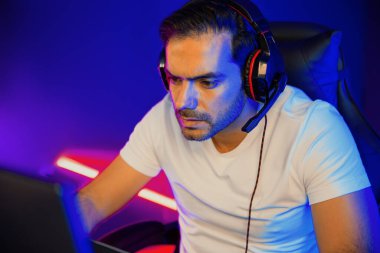 Akıllı oyun kurucusu, dijital neon ışıklandırma stüdyosundaki sosyal medya uygulamasında başkalarıyla iletişim kurmak için kulaklık ve mikrofon kullanan takım üyeleriyle konuşuyor. Tahmin et..