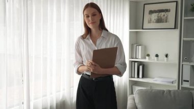 Klinikteki dost canlısı psikolog kadın. Profesyonel portresi. Kameraya bakıp psikolog muayenehanesine bakıyor. Tecrübeli ve kendinden emin psikolog.