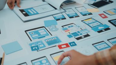 Ellerin renkli yapışkan notlar, dijital araçlar ve prototipleme sürecini geliştiren cihaz modellemeleri ile mobil uygulama tasarımına dahil olduğu yaratıcı çalışma alanının yakın plan görüntüsü. SACTR