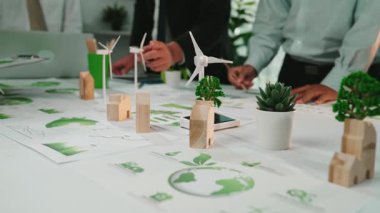 Sürdürülebilir proje planlaması, çevre dostu grafikler ve yenilenebilir enerji kavramlarını bitki ve grafiklerle dolu modern çalışma masalarında sergileyen çeşitli bir ekip işbirliği yapmaktadır. SACTR