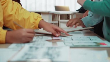 Çok canlı bir mimari stüdyo sahnesi çeşitli bir ekibin planlarını tartışırken takım çalışmasını ve tasarımda yaratıcılığı yansıtan karmaşık bir modeli incelediğini gösteriyor. SACTR