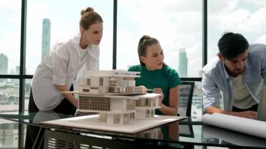 Beyaz proje yöneticisi dizüstü bilgisayar analiz verilerini kullanırken, mimar mühendis ekibi ev modeli inşaatını analiz etmek için birlikte çalışıyor. Bir grup tasarımcı ev tasarımı hakkında konuşuyor. İzleme