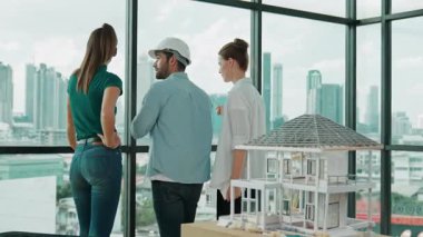 Gökdelene bakıp bir proje planı okurken, günlük kıyafetli akıllı mimar mühendis ekibi konuşuyor. Profesyonel yönetici takımı ev inşaatı hakkında beyin fırtınası yapıyor. Arkadan bak. İzleme