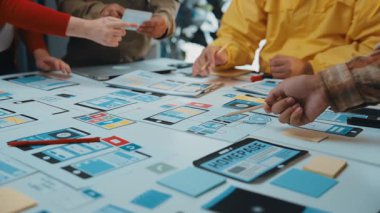 Dinamik bir ekip, renkli yapışkan notlar, akıllı cihazlar ve modern çalışma alanı masasındaki işbirlikçi beyin fırtınası araçlarıyla çevrili bir tasarım toplantısına katılır. SACTR