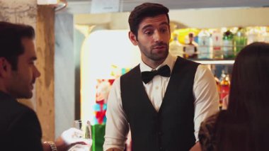 İyi görünümlü barmen hoş geldin içkisi veriyor. İçki tezgahındaki müşterilere dostça sohbetler ediyor. Temiz profesyonel barmen kostümünün içinde harika bir ilk izlenim bırakıyor. Vinosity.