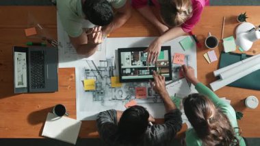 İnşaat mühendislerinin masa başında proje planıyla otururken tablet kullanarak ev yapısını dizayn etmelerine tepeden aşağı bir bakış açısı. Ekip planlama ve inşaat hakkındaki fikirlerin havadan görüşü. Sempozyum.