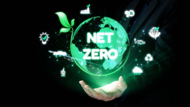 Yeşil parıldayan bir küreyi tutan bir el, sürdürülebilirlik, teknoloji ve çevresel sorumluluk sembolleriyle çevrili net sıfır hedef kavramını temsil eder. Dörtgen