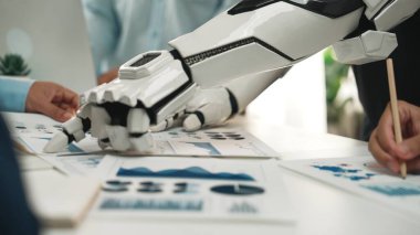 Çizelgeler ve grafiklerle dolu iş belgelerini incelerken insan eliyle uğraşan robotik bir kolu gösteren dinamik bir sahne. Noogenesis 'i simgeliyor.