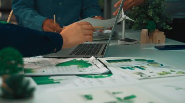 Modern bir ofis sahnesinde sürdürülebilirlik ve yeşil çözümler, belgeler, bir dizüstü bilgisayar ve aktif olarak tartışılan eller üzerinde odaklanmış bir ortak toplantı yer alıyor. SACTR