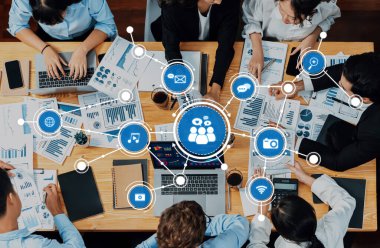 Modern ofis ortamında bir konferans masasında veri görselleştirmeleri, grafikler ve dijital cihazların yer aldığı dinamik bir iş toplantısı. Dostluk