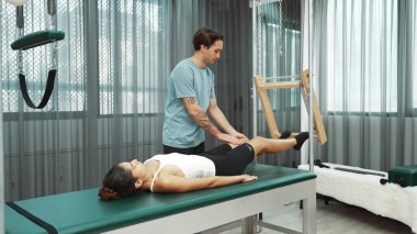 Pilates hocası, Cadillac teçhizatı üzerindeki bacak kaldırma egzersizi sırasında bir müşteriye yardım ediyor. Öğrenci uzanıyor ve temel dayanıklılık ve bacak esnekliğini arttırmak için Cadillac 'ın üzerinde bacak daire çiziyor. Alışkanlık.
