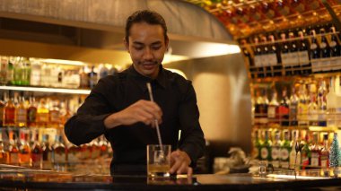 Zeki Asyalı barmen, bardakta karıştırılmış alkol şurubunu buzla karıştırıyor. Lüks gece kulübünde gece hayatı karışımı sergilenen özel bir içecek. Vinosity.