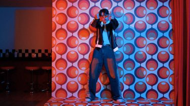 Asyalı break dansçı serbest stile geçiyor ve balon arka planlı kameraya bakıyor. Profesyonel hippi gündelik kıyafet giyer ve gözlük takar. Mutluluk.