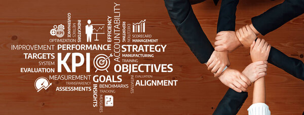 Разнообразная команда работает над бизнес-целями и ключевыми показателями эффективности. Изображение показывает руки, соединяющиеся над деревянным столом, символизируя командную работу и стратегию. Ах!