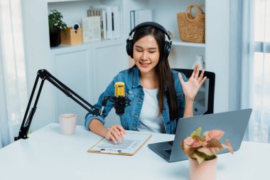 Sosyal medyada kulaklıkla canlı yayın yapan Asyalı sunucu modern stüdyoda yaşam koçluğu veya pazarlama dinleyicilerini selamlıyor. Taktik.