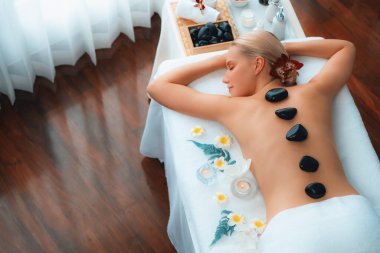 Lüks tatil beldesindeki kaplıca salonunda sıcak taş masajı. Gündüz huzurlu ortam, mutlu kadın müşteri bazalt taşı masajının keyfini çıkarıyor. Sessiz.