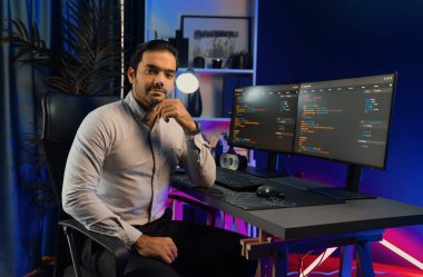 Bilgisayar ekranındaki yazılım geliştirme kodlamasına karşı poz vermek için akıllı bilişim geliştirici görünümlü kamera profilleri, neon ışıklı siber oda ofisinde program güncellemesi internet sitesi verileri sunuyor. Tahmin et..