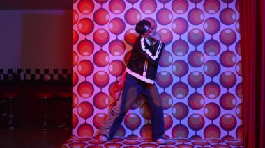 Asyalı break dansçı serbest stile geçiyor ve balon arka planlı kameraya bakıyor. Profesyonel hippi gündelik kıyafet giyer ve gözlük takar. Mutluluk.