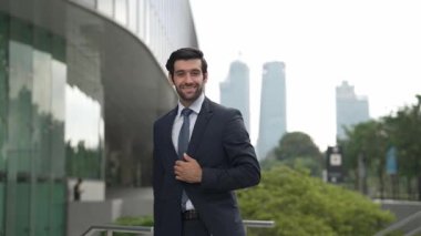 Profesyonel iş adamı hareket ediyor ve kameraya bakarken ayakta duruyor. Gülümseyen yönetici kameraya kendinden emin bir şekilde gülümsüyor. Mimari binada takım elbiseli yatırımcıların yakın çekimi. Sevinçli..