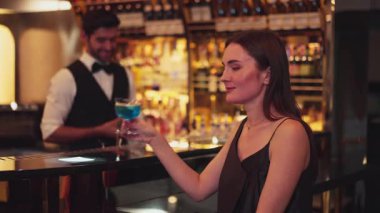 Güzel bayan konuk kameraya bakarak poz veriyor. Kulüpteki akıllı barmen geçmişi ile ilgili toplantı için lüks tezgah barında mavi Hawaii kokteyli ile karışık votka içiyor. Vinosity.