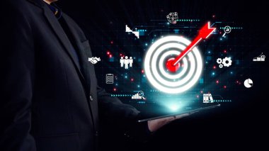 Bir işadamı, çeşitli iş analitik grafikleri, strateji, yönetim ve teknoloji entegrasyonunu sembolize eden bir hedef ikonu gösteren dijital bir tablet tutuyor. Dörtgen