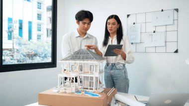 Güzel, genç, beyaz bir proje yöneticisi Asyalı mühendise, mühendislik masasında ev modelini ölçerken tablet kullanarak bina detaylarını anlattı. Tertemiz.