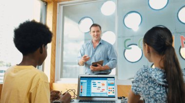 Akıllı öğretmen tableti elinde tutarken, öğrenci de bilgisayar ve elektronik ekipmanlarla mühendislik kodlarını öğreniyor. Mutlu çocuklar program yazmak için birlikte çalışıyorlar. Öğretim.