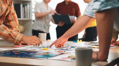 Hareketli bir ofis sahnesi aktif olarak bir takım toplantısına katılan elleri resmediyor. Masanın üzerine renkli çizelgeler ve yapışkan notlar sergileniyor, işbirliği ve fikir paylaşımı gösteriliyor. SACTR