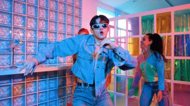 Asyalı adam gece kulübünde çeşitli neon ışıklarda dans ederken kolunu oynatıyor. Modern kulüpte çok kültürlü hippilerle dans eden şık elbiseli mutlu dansçı. Mutluluk.