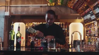 Güzel görünümlü Asyalı barmen içki şurubunu kullanarak lüks içki tezgahında cam hazırlama, gece kulübü lüksündeki düzgün profesyonel barmen kostümü yapıyor. Vinosity.